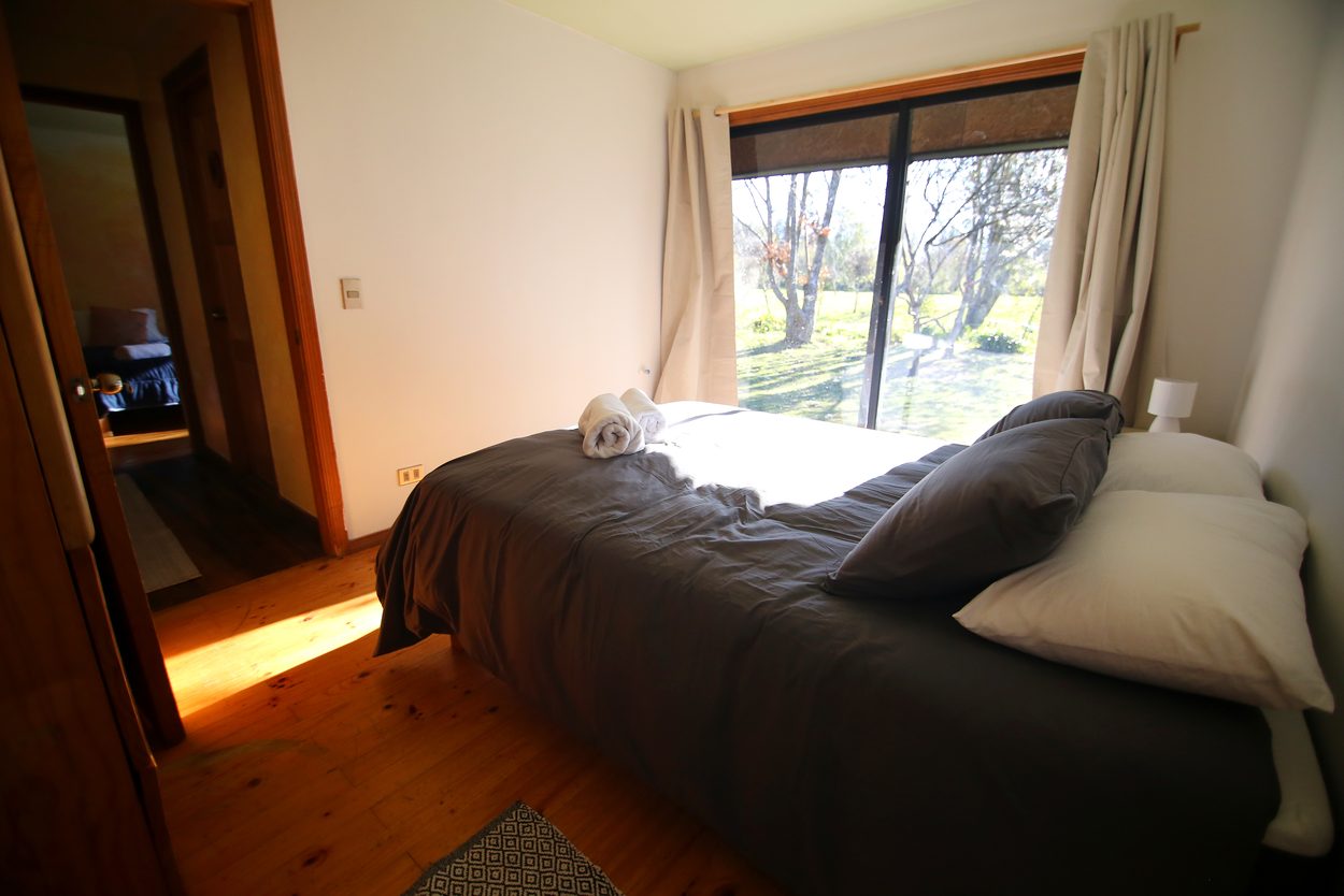 Cama matrimonial junto al ventanal que da al jardín