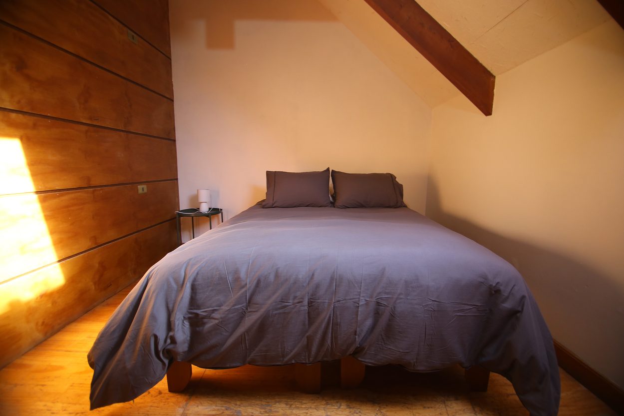 La cama matrimonial contra el muro de madera del segundo piso